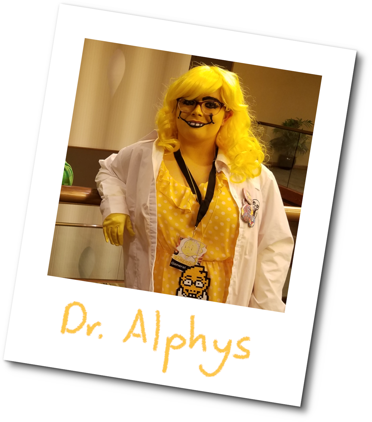 A woman cosplaying as Alphys from Undertale stands leaned up against a railing in a fancy venue. She wears a curly, bright-yellow wig, purple-rimmed eyeglasses, a yellow and white polka-dotted dress covered with a labcoat, and yellow gloves. A lanyard hangs from her neck with a sticker of Alphys and the word 'Nerd' on it, perler bead art of Alphys hanging from her neck to show what character she was to the world, and her labcoat is adorned with Undertale pins. Her face and neck are coloured with yellow face paint, and teeth have been drawn over her lower lip to mimic Alphys's buck-toothed smile. Her eyebrows have been filled in with black, and her eyelashes enhanced in order to mimic Alphys's cartoony look. The picture is surrounded by a polaroid frame, and signed with 'Dr. Alphys' in yellow pencil.