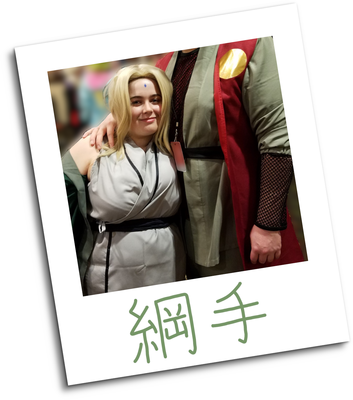 A woman wearing a storebought Tsunade cosplay stands next to a Jiraiya cosplayer, whose head has been cropped out of the frame for privacy. The background has been blurred out in GIMP. The photograph has been framed to look like a polaroid, and is signed with the name '綱手' (Tsunade in English) in green ink.